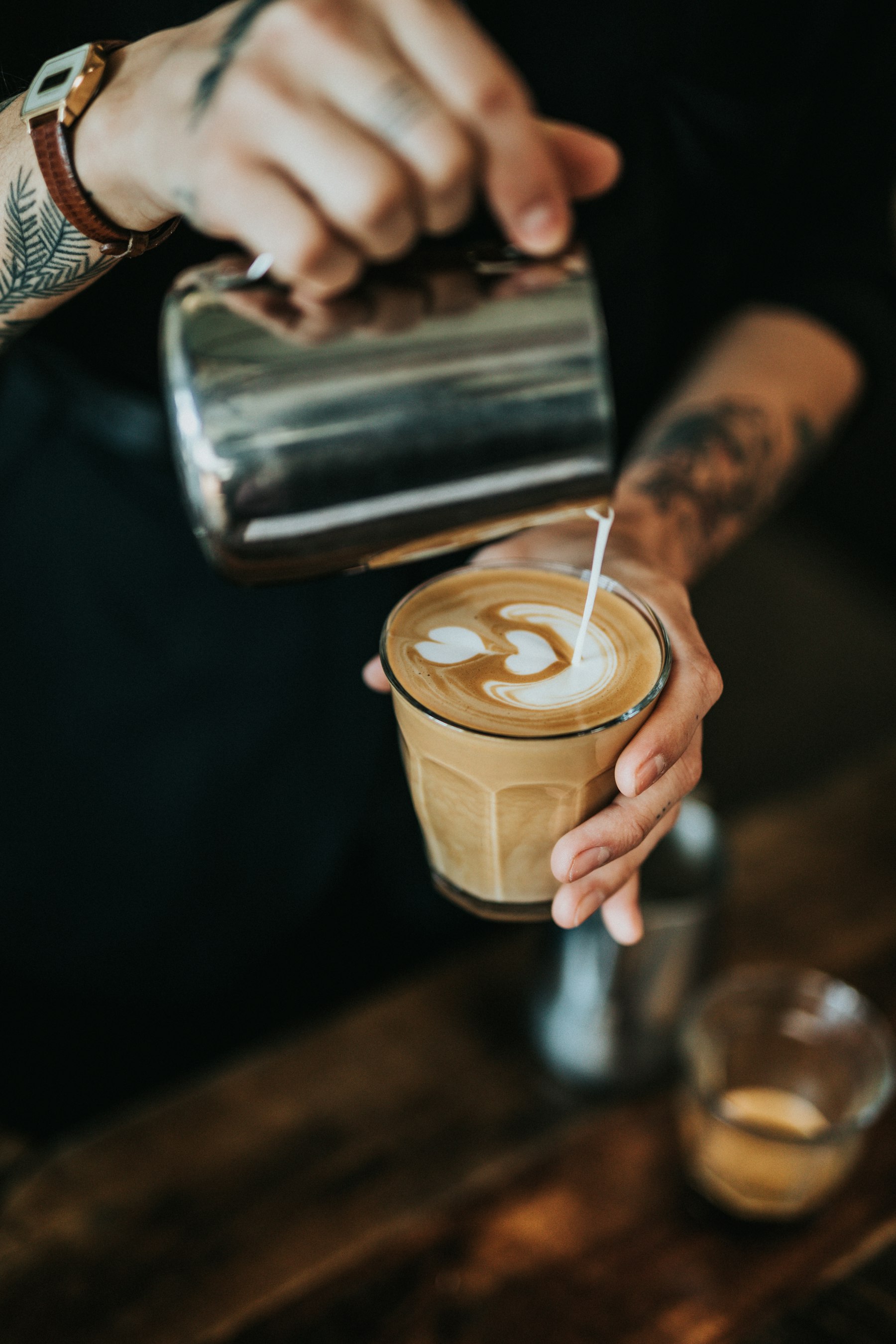A tattooed barista pouring latte art into a glass