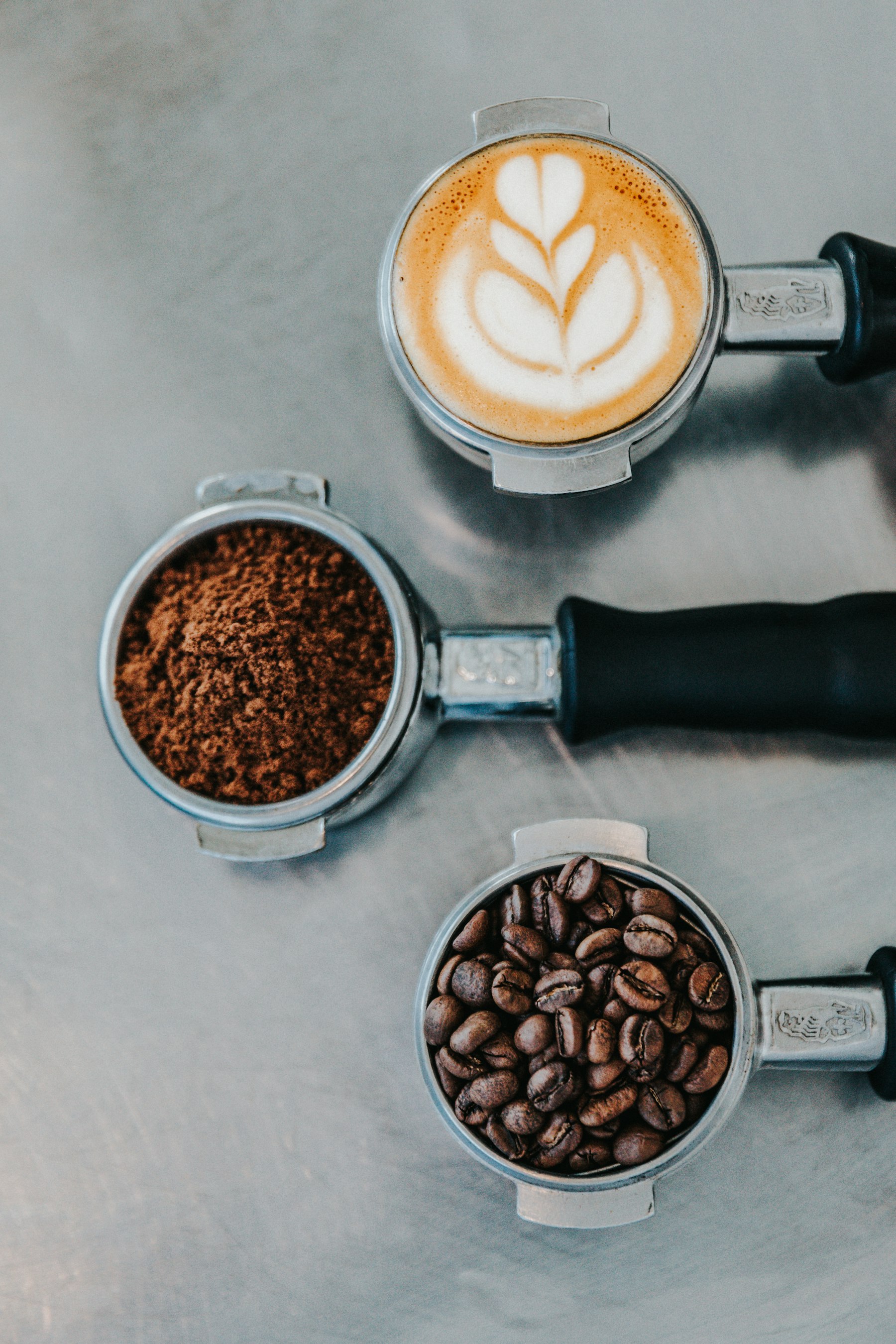 Three portafilters holding roasted beans, ground coffee and a finished flat white